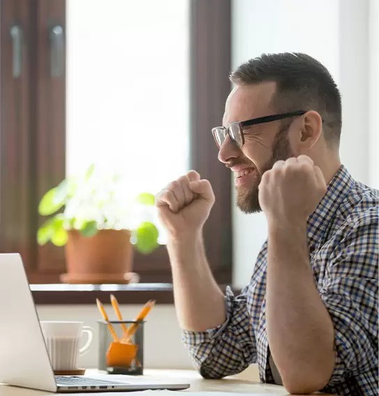 A guy working on a laptop, hands raised in a celebratory fist-pump, cheering after realizing he avoided a mistake.