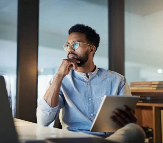 A thoughtful professional with glasses, deeply concentrated on his work as he gazes at his laptop screen.