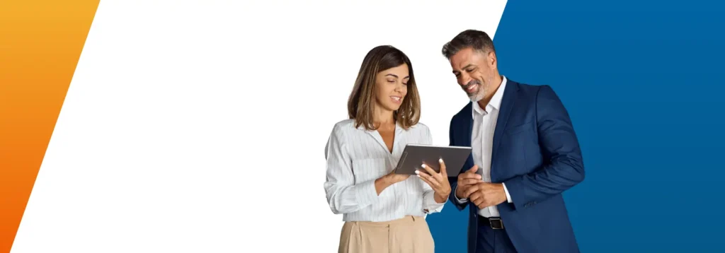 A professional man and woman engaged in a discussion, using a tablet device.